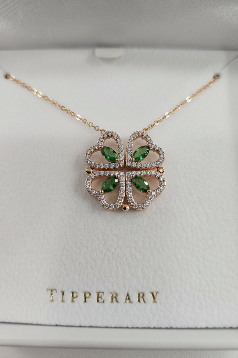 A gold-tone four-leaf clover pendant necklace with light green marquise-cut gemstones and small clear stones, displayed on a white Tipperary jewelry box.